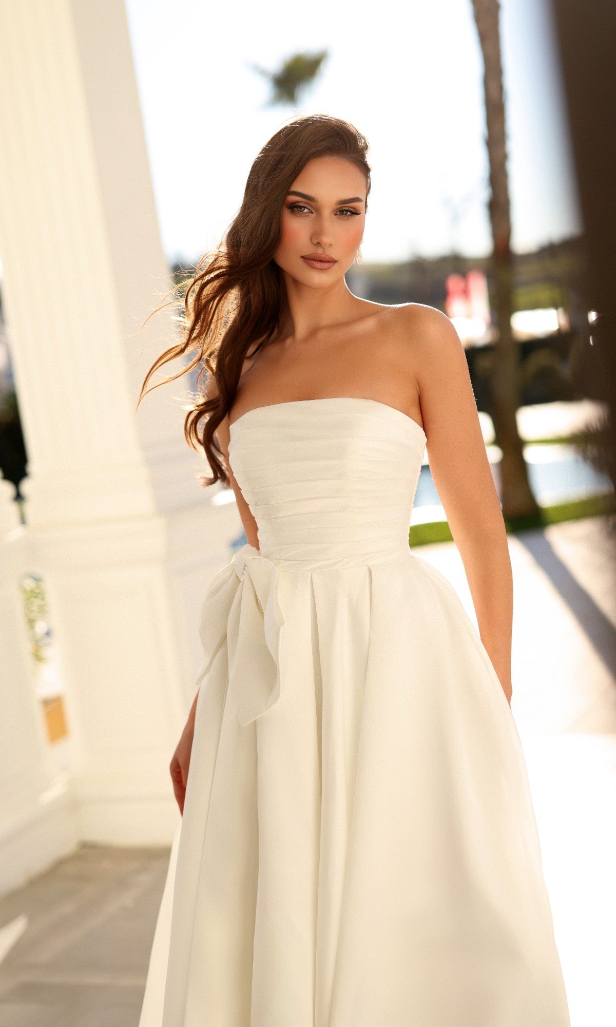 Tina Holly TW621 long wedding dress, a strapless white gown featuring a fitted bodice, pleated skirt, and a bow tie at the waist.